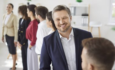 Happy smiling confident man company employee in formal clothes looking cheerful at camera with a team of successful colleagues standing in a row in modern office. Business portrait concept.