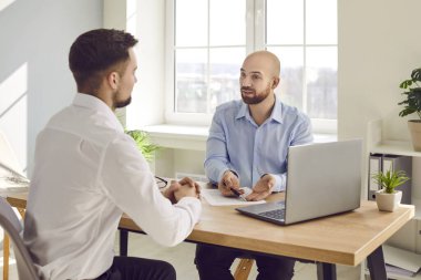 Two serious business men sitting at the desk of workplace talking and discussing financial report in office. Male company employers considering new projects, analyzing company. Team work concept.