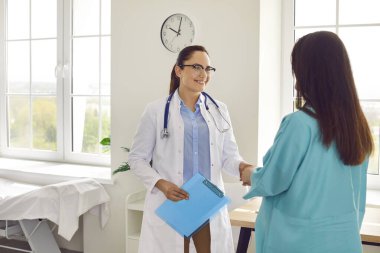 Happy, smiling doctor supports a pregnant woman patient. Friendly obstetrician with a clipboard meets and exchanges handshakes with a young pregnant girl. Pregnancy, health care concept