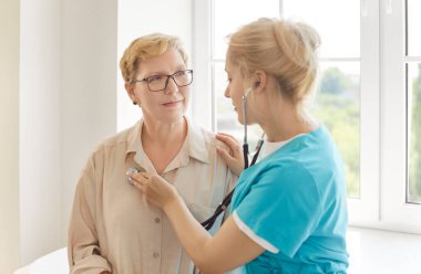Nurse using stethoscope to diagnose elderly patients heartbeat and lungs in clinic. Professional medical care by doctor, disease prevention and health checkup for senior woman in hospital