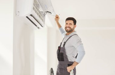 Happy smiling worker handyman man installing attaching air conditioning unit, AC repair, room temperature control, adjust optimal device performance, professional or technician providing ideal climate