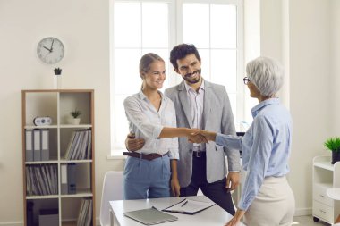 Handshake of bank agent and young family after successfully signing documents in bank office. Female manager congratulates customers on successful deal. Concept of financing and lending.