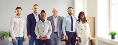 Group of business multiethnic people men and women looking at camera and smiling indoors. Company employees team or group of staff standing in office confidently. Business people portrait. Banner.