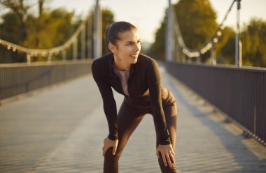 Şehir parkındaki spor salonunda güzel bir kadın. Modern spor kıyafetleriyle genç, zayıf, çekici bir kızın portresi köprüde dizlerinin üzerine çöküp başka tarafa bakıyor. Spor konsepti