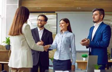 Başarıyı kutlayan iki kadın el sıkışıyor, anlaşma yapıyor, iş başarısı ya da işyerleri için sözleşme imzalıyor. Bir grup iş adamı iş arkadaşlarını alkışlıyor..