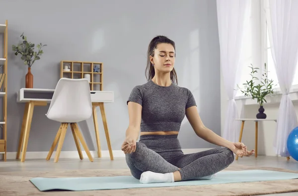 A young woman sits on the floor in the lotus position at home. A beautiful girl in sportswear does yoga. Concept morning practice, keep fit, concentration and balance, meditation