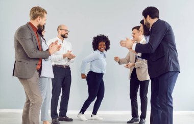 İş arkadaşları ofiste alkışlarken Afrikalı Amerikalı iş kadını dans ediyor. İnsanlar parti sırasında bir başarıyı kutluyor, canlı ve destekleyici bir çalışma ortamını vurguluyorlar..