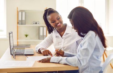 Gülümseyen mutlu iş kadını Afro-Amerikan kadın bir anlaşma yaptı ve çalışma masasında oturan bir sözleşme imzaladı genç bayan iş arkadaşı veya iş ortağı ile anlaşmaya vardı..