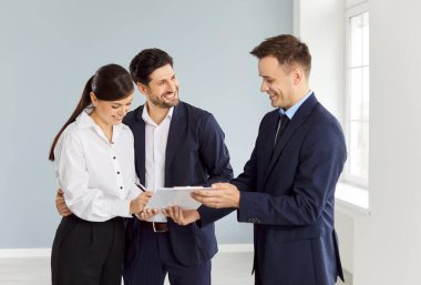 Happy man and woman signing a document in an empty room, close-up. The real estate broker enters into an agreement with the couple. Bank loan to buy a house, mortgage, rent an apartment