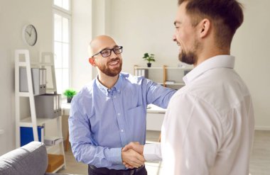 Two happy smiling men shaking hands standing in office finishing meeting, celebrating success, business achievement, making a good deal, , signing a contract or greeting new employee.