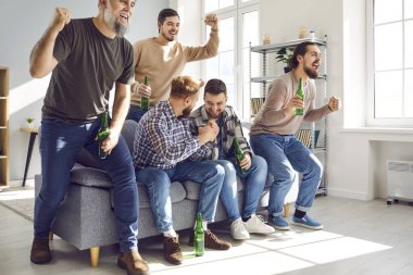 Group of football fans watching sport match on TV together. Emotional male friends sitting on sofa drinking beer and celebrating victory of their team at home. Friendship, entertainment concept