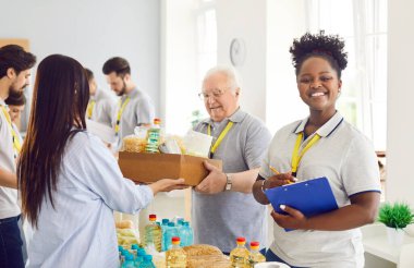 Multiracial volunteer diverse group, african american woman working in charitable food foundation, donation to needy, separating food bank stocks, basic need provisions, free meal for people in need