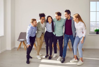 Group of happy business team hugging looking at each other. Overjoyed diverse successful employees, business partners or happy friends standing together modern in office