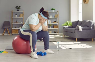 Fat woman cant lose weight despite her sports workouts. Sad, frustrated, exhausted, overweight, chubby, plump, young woman sitting on fitball in living room, hiding her face in hands, and crying