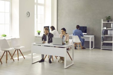 Busy people in office. Modern interior of companys workplace with employees sitting at tables with laptops. Business colleagues working in office or coworking space. Successful business concept.