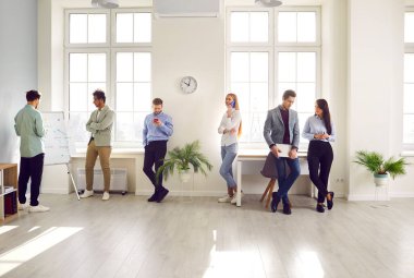 Business professionals at a modern workplace. Several diverse employees working in the office. Young multiracial men and women standing in the office, communicating, discussing work, talking on phones