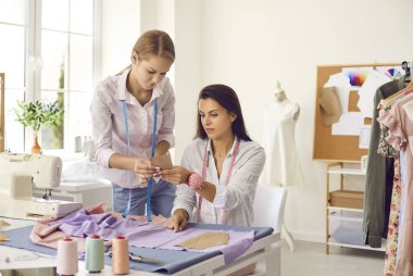 Kadın terziler kişisel moda atölyesinde müşteri kıyafetleri üzerinde birlikte çalışırlar. Kadın terziler ya da tasarımcılar atölyede birlikte tasarım giysileri dikerler. Moda ve terzilik konsepti. Küçük işletme.