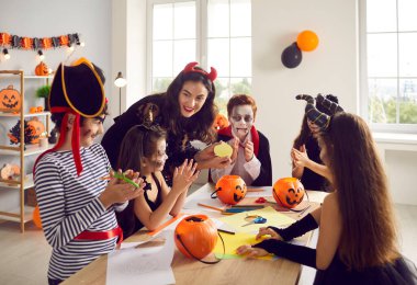 Playful teacher learn together with children celebrate Halloween in school. Smiling tutor study have creative art activity with kids on all saint eve in kindergarten. Fall October scary masquerade.