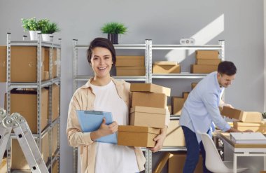 Kadın yönetici elinde karton kutularla lojistik ya da dağıtım merkezinde çalışan erkek meslektaşıyla depodaki depoda müşteri siparişi hazırlıyor. Envanter ve teslimat konsepti.