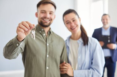 Happy young couple holding keys to new apartments, close-up. Real estate agent looking at happy man and woman. Concept new apartment, real estate, giving keys, hand holding