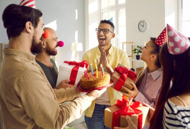 Happy diverse friends greeting with cake and presents excited African American guy. Caring smiling young people congratulate smiling biracial mate with birthday anniversary. Celebration concept.