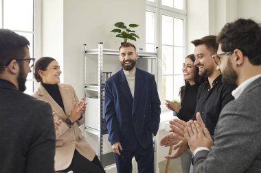 Group of employees and coworkers applauding the smiling young business man with beard and mustache in the office. Business team or group of staff congratulating their leader making a successful deal.