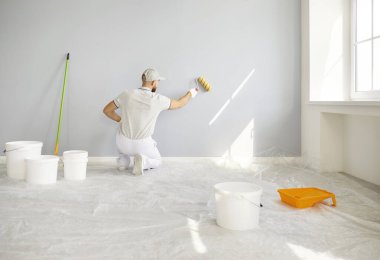 Painter or construction worker wall painting sitting rear, professional service team worker wearing protective white uniform, preparation, painting with paint roller brush tool, covering surface