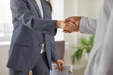 Two diverse business women in suits meet and exchange handshakes. Professional therapist with clipboard shakes hands with patient. Woman hiring manager congratulates new employee after job interview