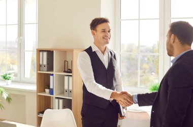 Two happy smiling men shaking hands standing in office finishing meeting, celebrating success, business achievement, making a good deal, , signing a contract or greeting new employee.