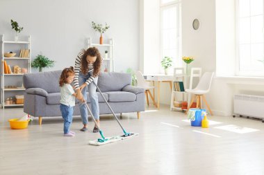 Happy playful funny active family, little helper, domestic chores game mother parent, babysitter and cute small child daughter together in living room interior, kid fun learning to enjoy leisure home