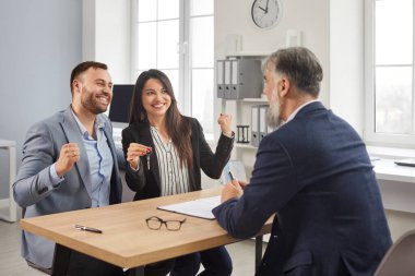 Couple getting key to new house or apartment from realtor. Happy homeowners buying or renting their new home and receiving keys from male realtor. Family buying property, mortgage investment