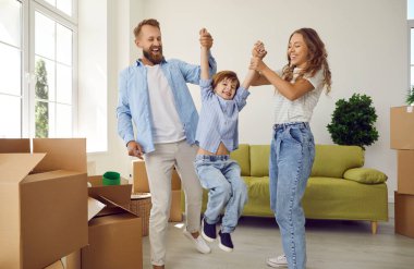 Happy young Caucasian parents play with small child unpack on moving day to new home. Overjoyed family with kid celebrate relocation to own house. Bank loan or mortgage, rental, real estate.