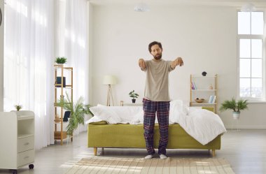 Sleepwalking. Somnambulist man gets out of bed in morning with closed eyes and outstretched arms. Young Caucasian man in pajamas walks like sleepwalker in bedroom. Sleep disorder concept.