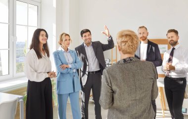 Group of business people chatting on a meeting standing in office. Company employees discussing work project. Confident coworkers listen to their colleague. Corporate business team concept.