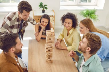 Bir grup mutlu genç kız ve erkek evde ahşap yapı taşlarıyla birlikte oynuyorlar. Masada oturup birlikte eğleniyorlar. Ev eğlencesi ve masa oyunları konsepti.