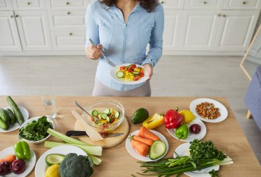 Overhead shot of woman v vegetable salad on table in kitchen at home, focusing on healthy food and diet, enhancing wellness in a domestic space designed for culinary preparation and nourishment.