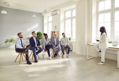 African American businesswoman trainer, coach training employees in office. Female speaker standing against of sitting people giving educational workshop, teaching business team at corporate meeting