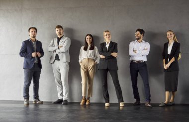 İş adamları ya da iş arkadaşları, resmi kıyafetler giymiş gri duvara karşı duruyor. Önemli konuları görüşmek için ofiste buluşuyorlar. Kapalı alanda başarılı yardımcı personel