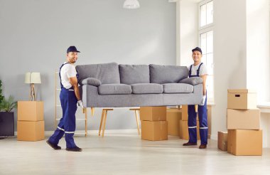 Movers male professional team in overalls loading, place furniture sofa at new location with care, pack and unload items, physically fit happy loader service men working, delivery 
