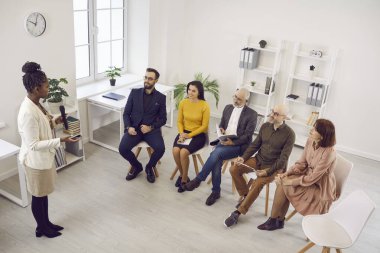 African American female coach or speaker talk lead meeting with diverse multiethnic colleagues in office. Black businesswoman speak in microphone head presentation or training for employees.