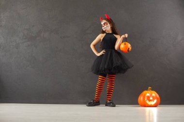 Small girl child in costume with jack-o lantern isolated on black background celebrate Halloween scary holiday. Little kid act play as evil witch for All Saints Eve fall celebration in kindergarten.