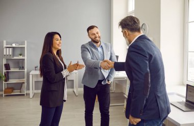 Business partners handshaking in office while female colleague applauding them. Happy businessmen shaking hands to close deal. Boss handshaking man employee thanking for good work results