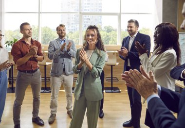 Smiling young attractive woman proudly looking at camera with team of people applauding in office. Business team or group of staff congratulating their leader on a meeting or conference.