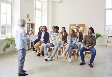 Çeşitli iş adamlarından oluşan bir grup, iş projesini görüşmek için ofiste sırayla oturuyorlar. Şirket çalışanları konferans odasında olgun bayan meslektaşlarını dinliyorlar..