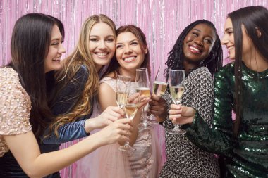 Five diverse women dressed in elegant dresses, celebrating Christmas or New Year party together, holding champagne glasses filled with sparkling drinks, raising them in toast in festive atmosphere