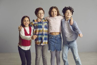 Studio portrait of huddling and smiling bunch of kids. Group of four happy little school children standing in row and hugging each other. Cheerful preteen friends having fun together