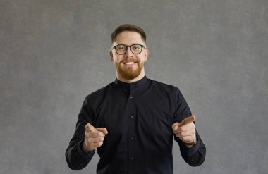Positive successful man makes finger guns, pointing directly at the camera, saying I choose you. Man stands on the background of a concrete wall and smiles contentedly finding a great candidate.