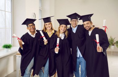 Portrait of smiling diverse students in mantles and hats pose with diplomas celebrate university graduation. Happy college graduates in robes excited with high school finish. Education concept.