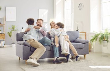 Young parents having fun with their children, hugging each other and playing together on sofa. Happy family spending quality time at home and enjoying their free time in living room during weekend.