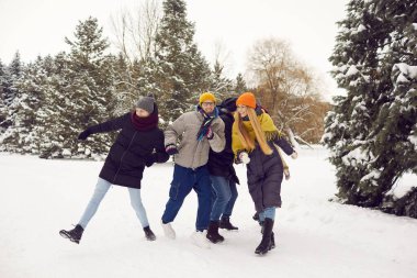 Group of cheerful active millennial friends in warm clothes walking in a winter forest. Happy young people gather in the park together, have fun and enjoy outdoor activities